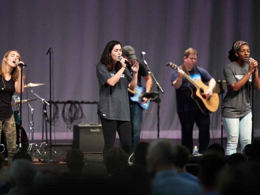 Students sing into microphones on a stage